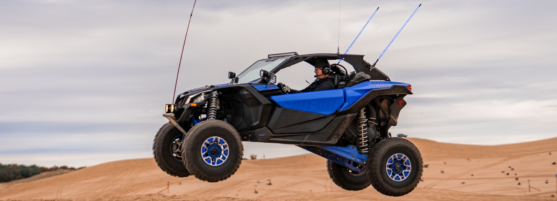 profile view of blue can-am maverick driving in sand