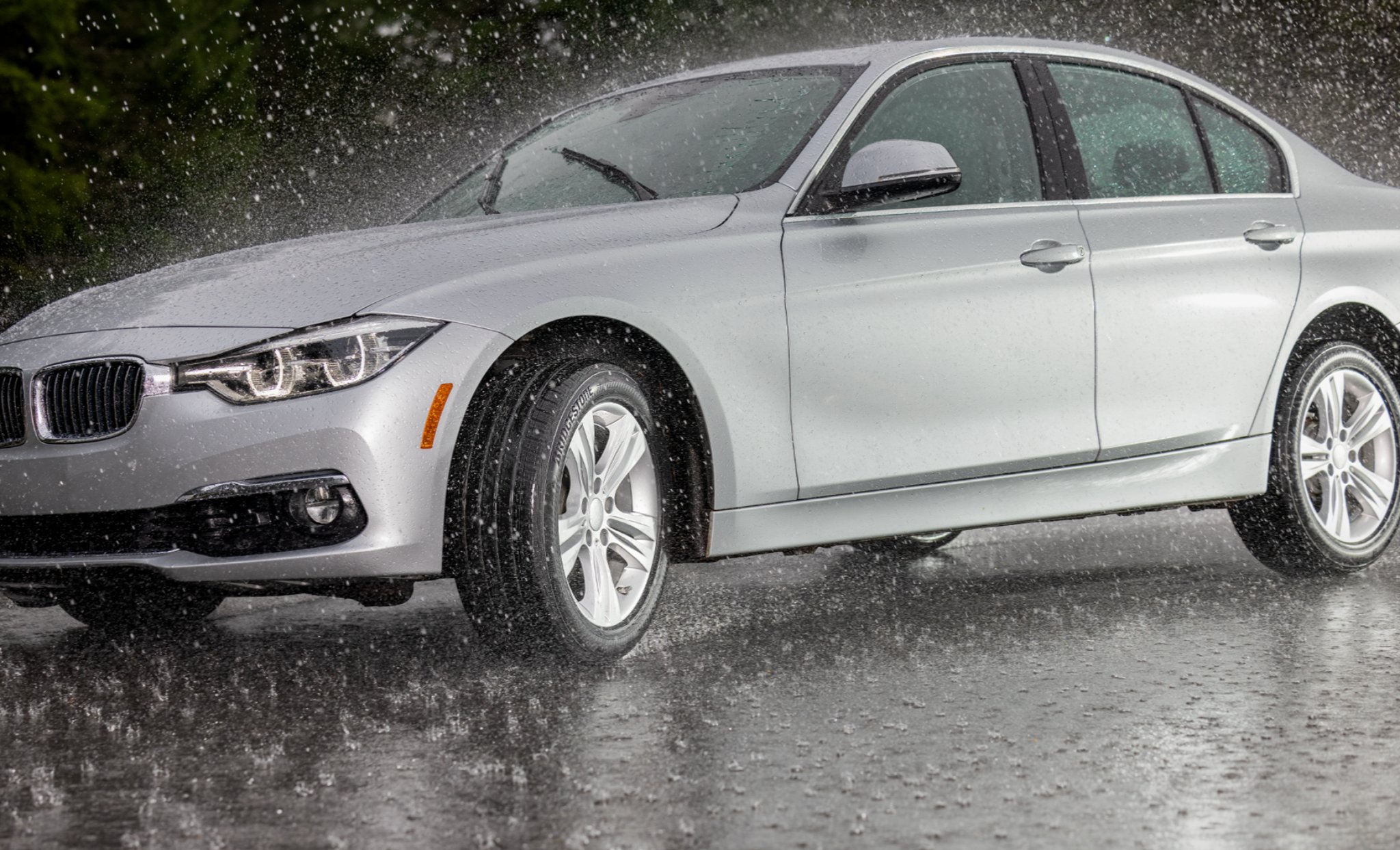 Silver BMW sedan driving on a wet road in heavy rain with run-flat tires