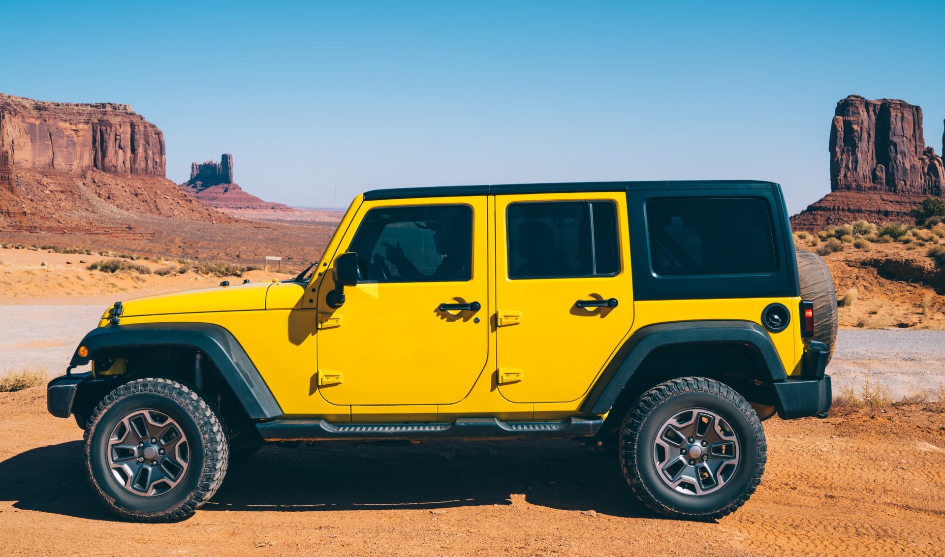 Yellow Jeep Wrangler parked at a side profile in the desert with rock formations in the background