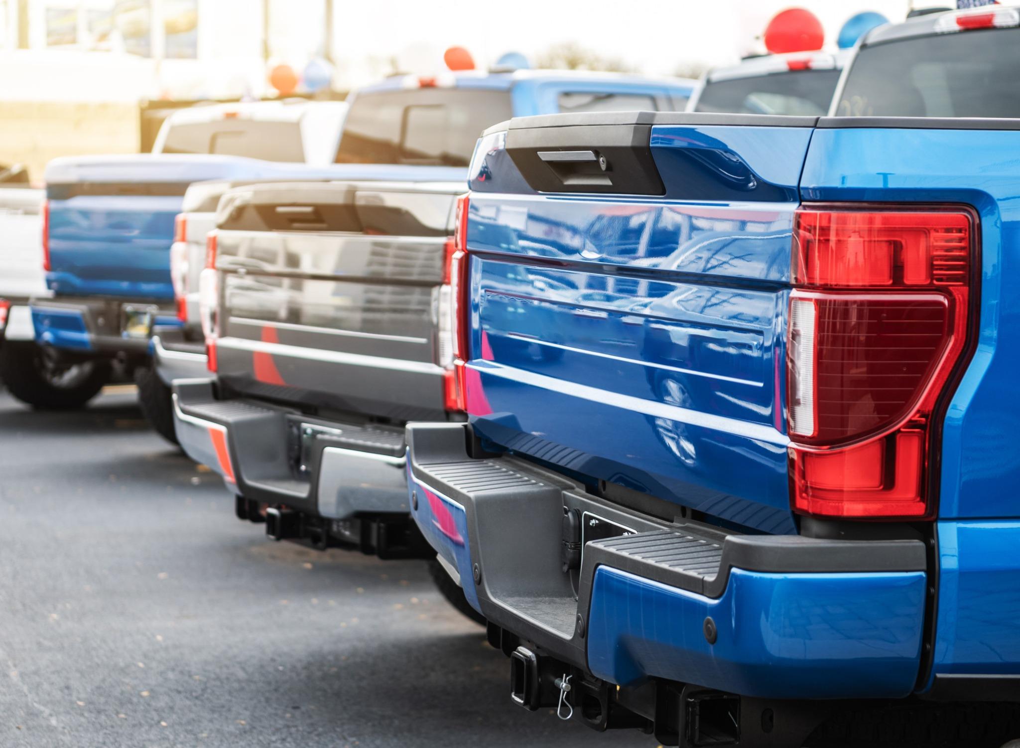 Several Ford F-150 trucks lined up in a parking lot, of varying colors from a rear angle