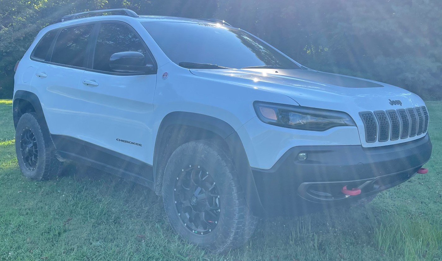 front view of white jeep cherokee in field with sun shining in background