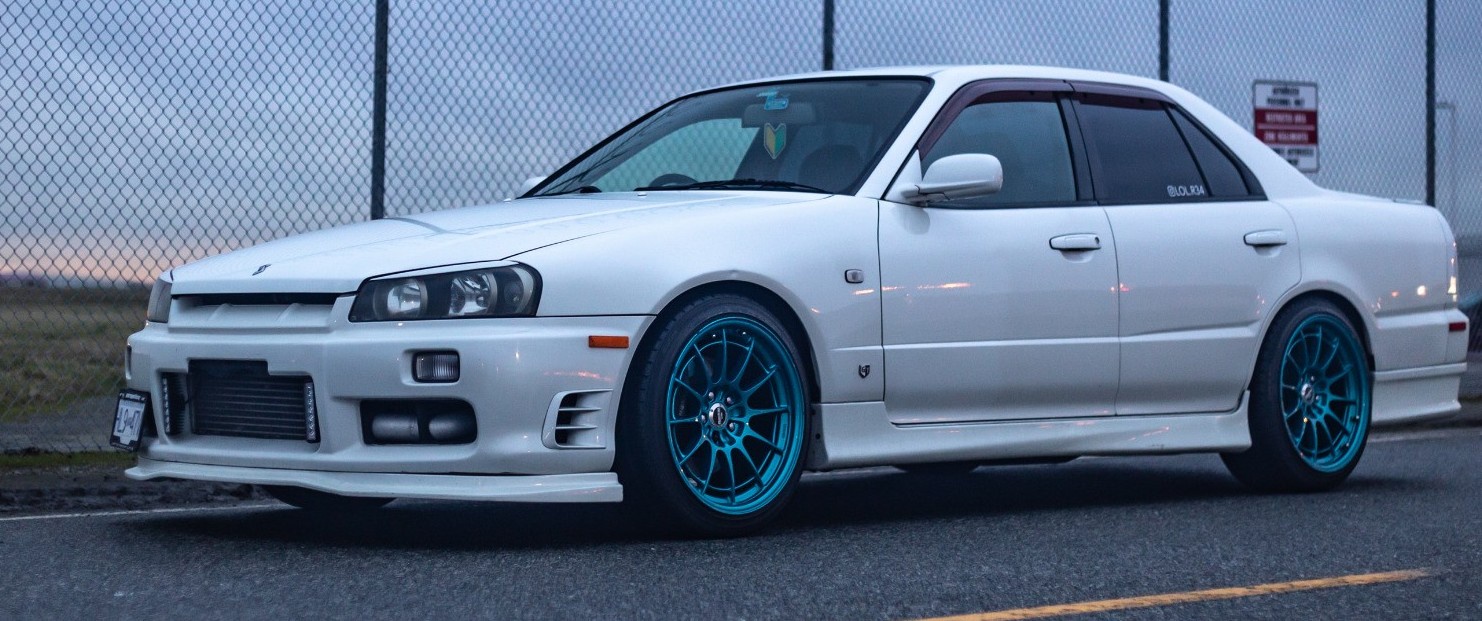 profile view of white nissan skyline r34 parked in front of airport